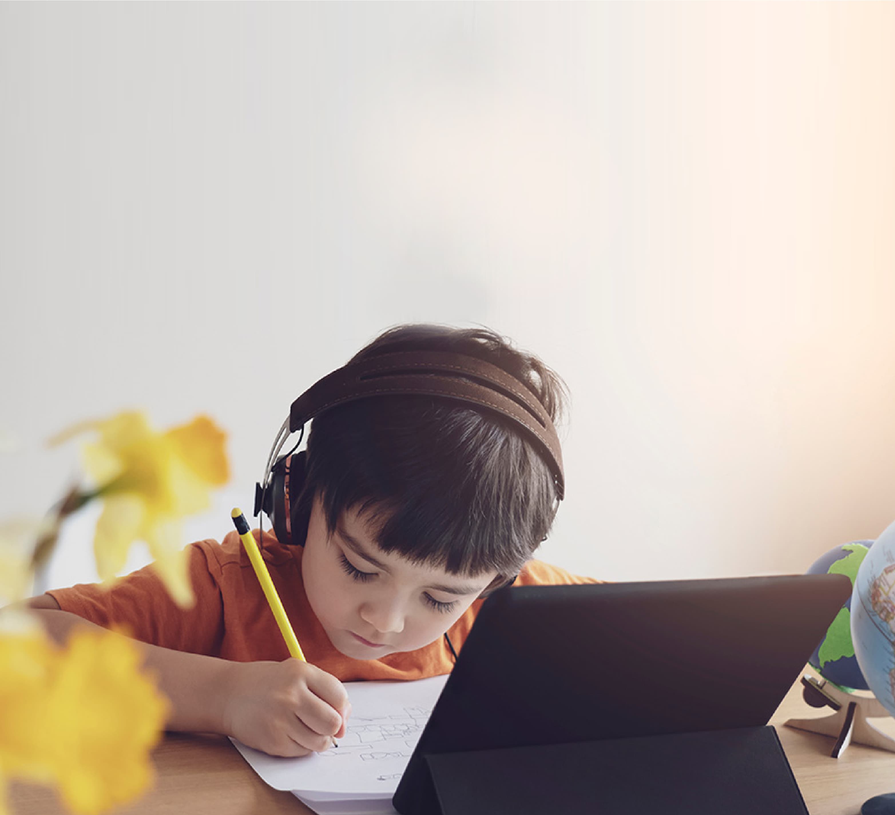 Child wearing headphones writing notes in front of a tablet