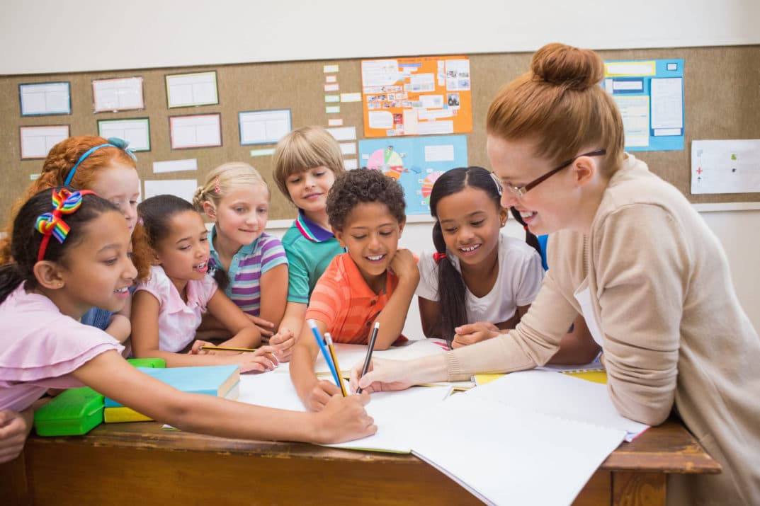Teacher helping a group of smiling students with their work